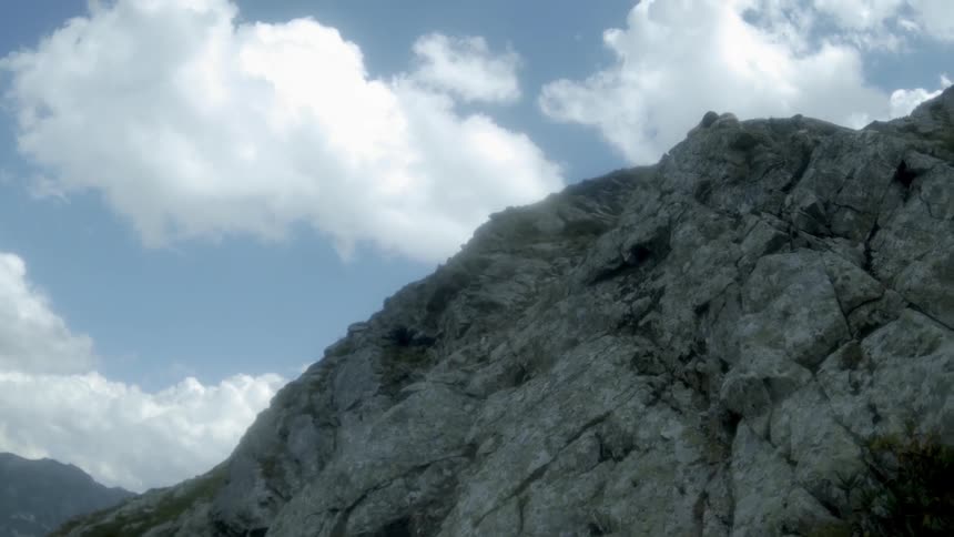 White clouds hang above a tall stone mountain