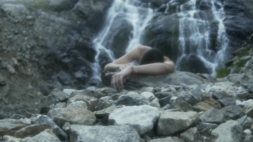 A man is passed out near a waterfall in the mountains