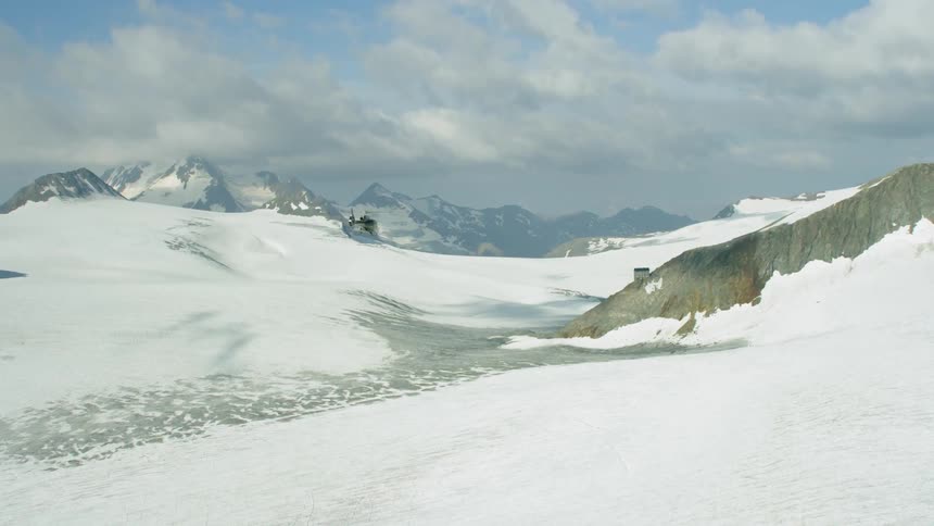 A helicopter is piloted over snowy mountains