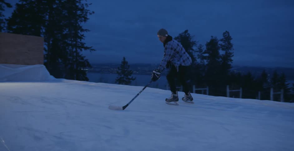 A man playing ice hockey outside at night and scoring a goal