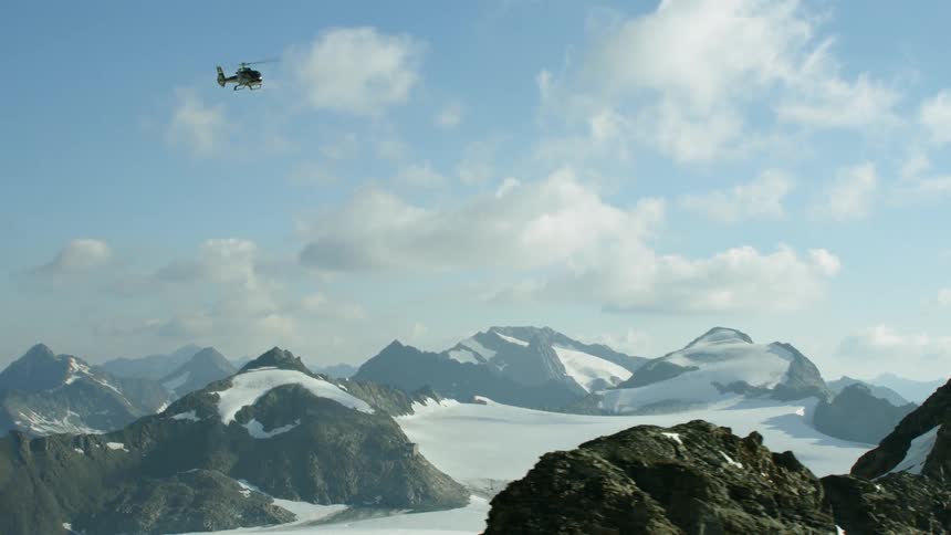 A helicopter is flying above a mountain range in daylight
