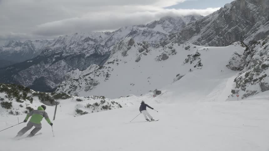 Two skiers are skiing down a mountain slope during the day