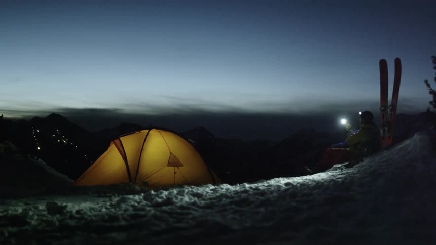 Travelers sit next to skis and a tent in snowy mountains
