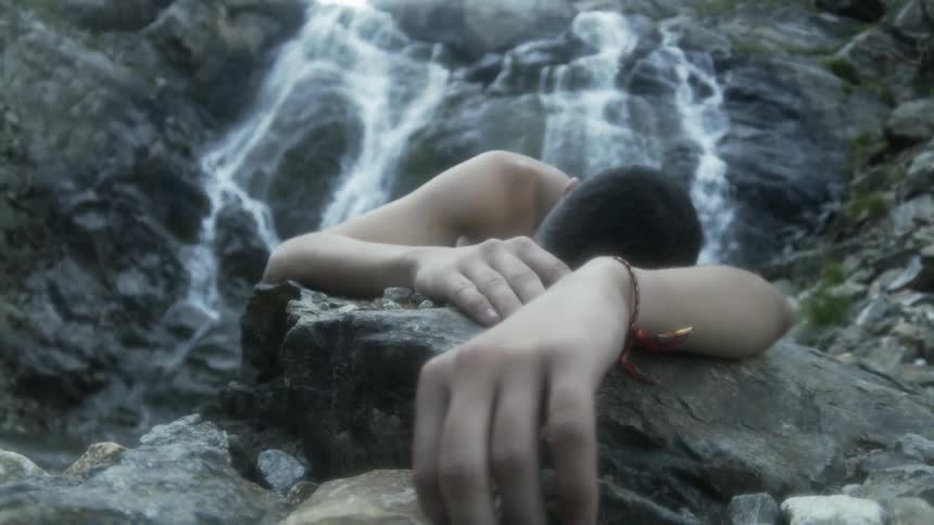 A young man lays on rocks by a waterfall