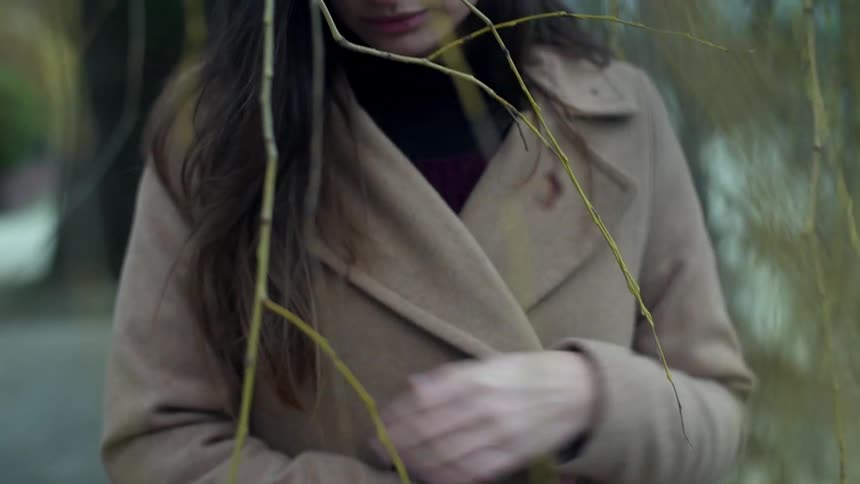 A woman is wrapping her coat around herself as she stands outside during the day