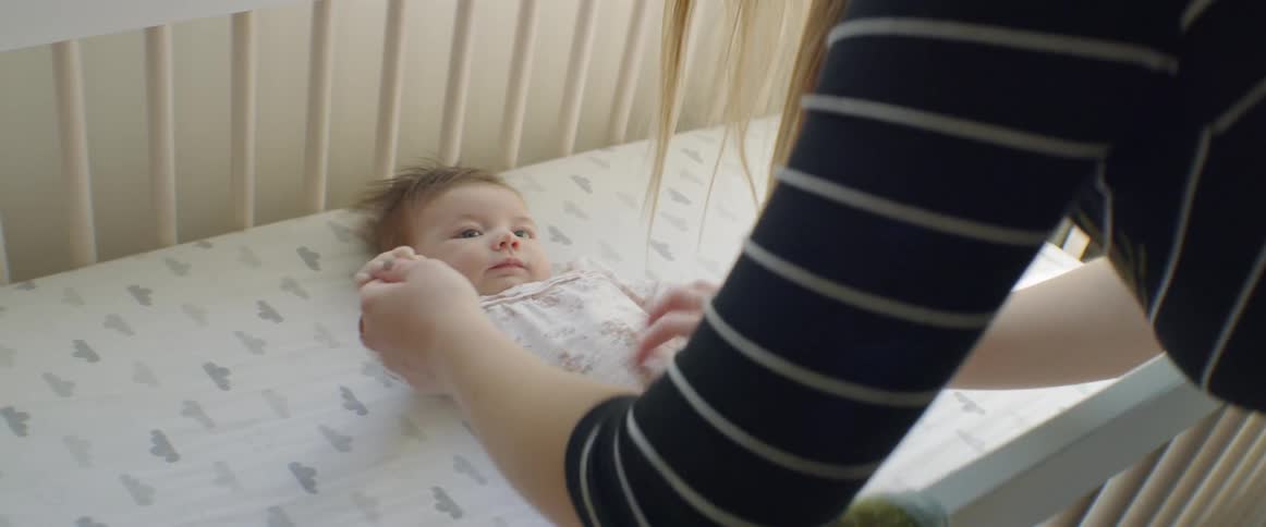 A woman leans over a crib and plays with a baby