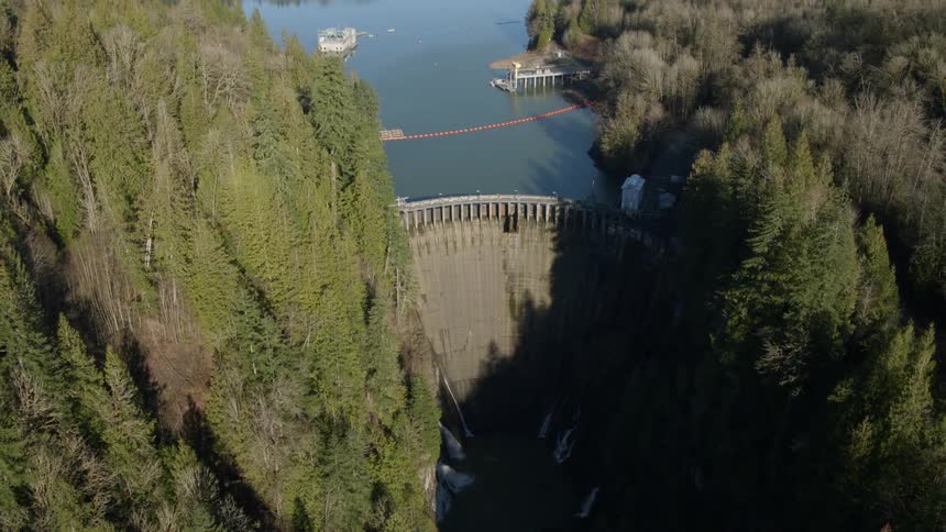 Tilting up from a deep river gorge to reveal a dam and reservoir surrounded by forest and mountains