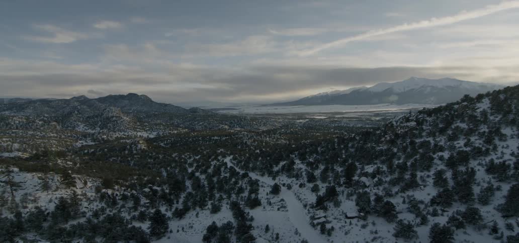Snow covers the road around the tree covered hill