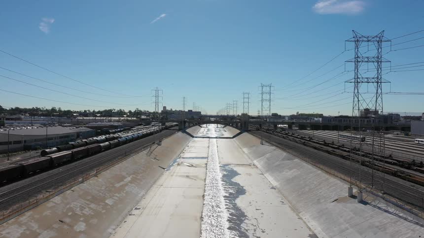 Water is flowing through a canal near a train yard on a sunny day