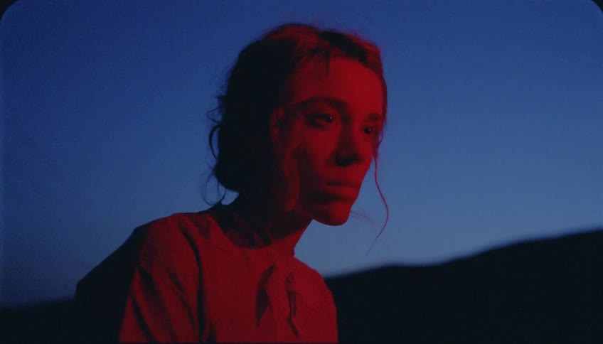 Red light glows on a woman's face outside at dusk