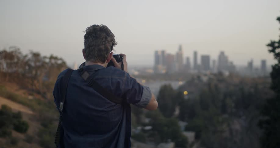 Photographer stands on a hilltop taking pictures of a city