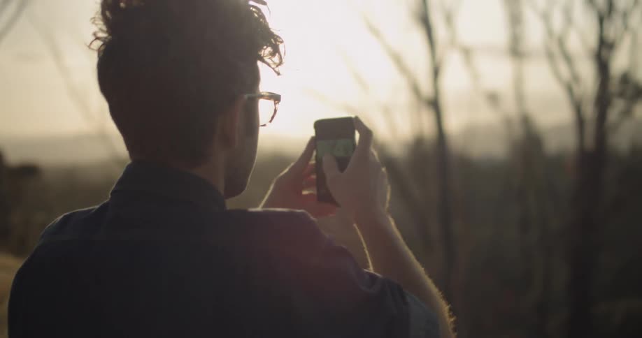 A man uses his phone to take a photograph during sunset