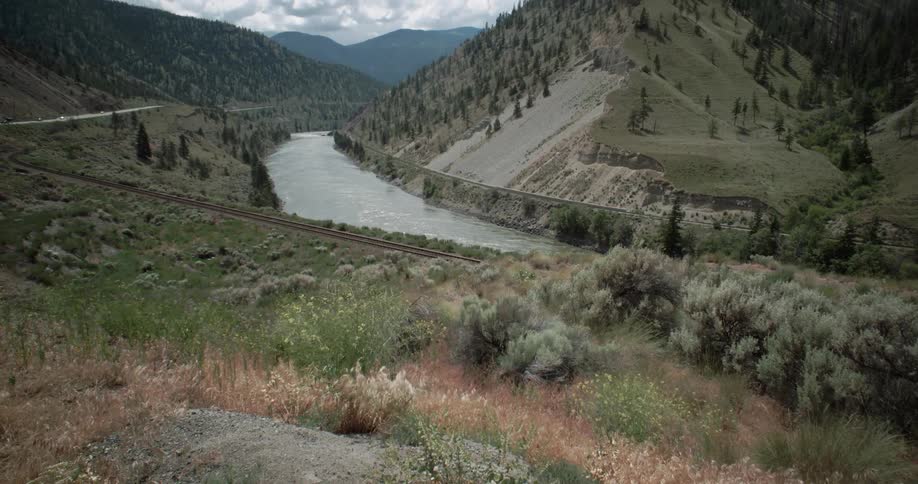Train tracks and a road at the base of a hill overlooking a river