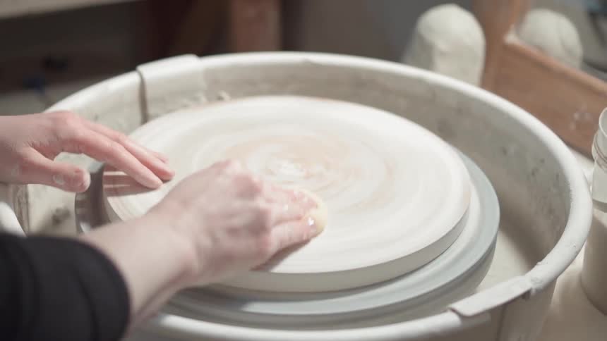 A woman is wiping down the surface of a pottery wheel during the day