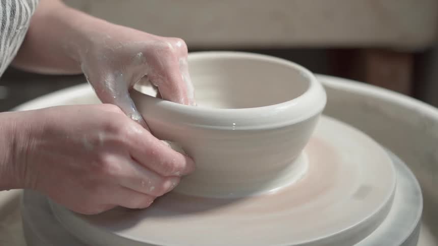 A woman is forming a bowl on a pottery wheel during the day