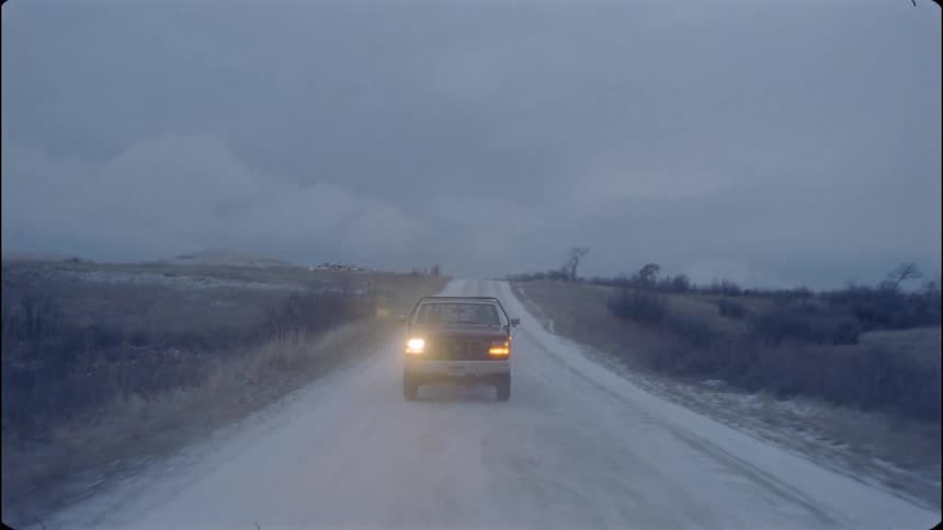Vehicle with its headlights on travels down a dirt road