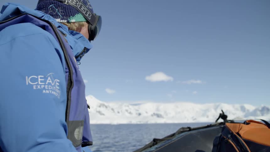 A man rides in a boat near snowy mountains