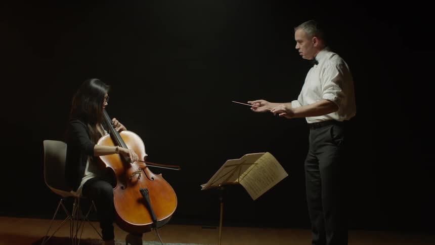A man conducts a woman playing a cello