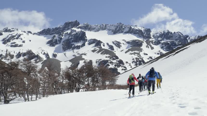 Group of people wearing skis walk towards snowy mountains