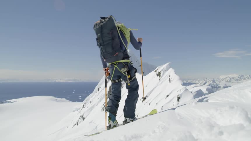 Man kicks snow off his skis on top of a snowy mountain