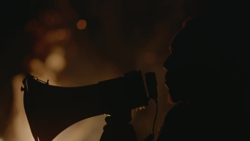 A man yells into a bullhorn near a bonfire