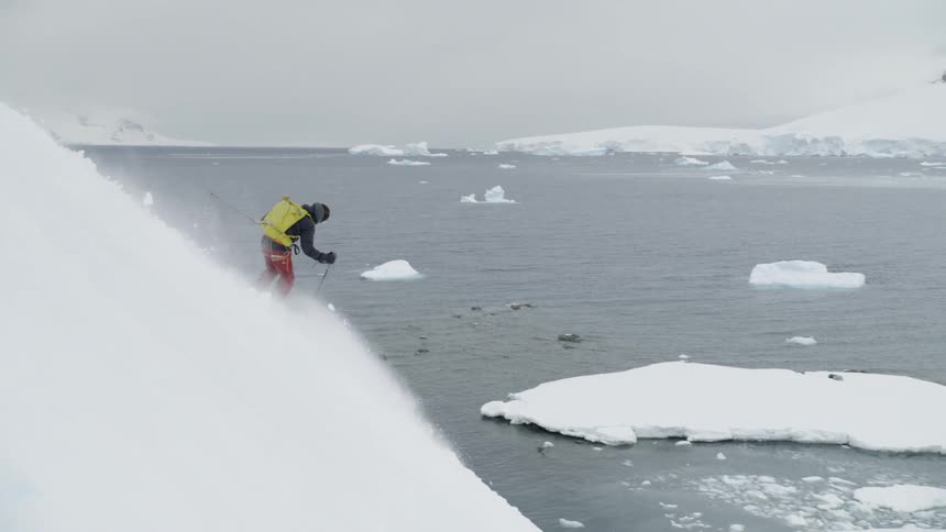 Person skis down a steep snowy mountain near a lake