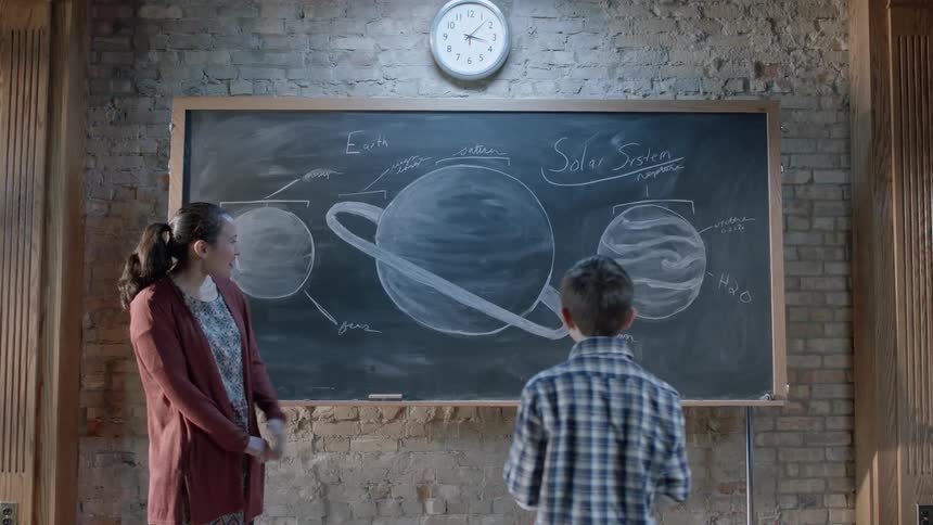 A boy approaches a teacher and the chalkboard after being called on