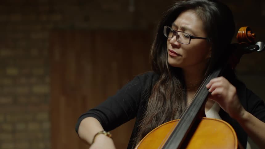 A woman is playing a cello inside on a stage
