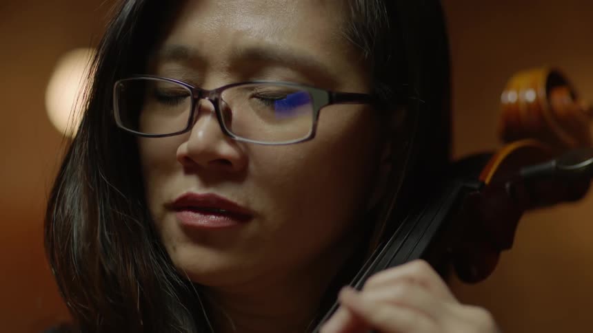 A woman plays a cello with her eyes closed