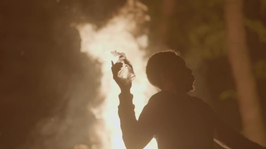 Man throws a glass bottle into a blazing fire