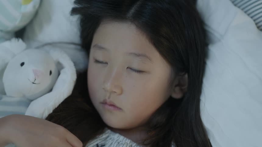 Little girl lays on her bed while cuddling a stuffed bunny