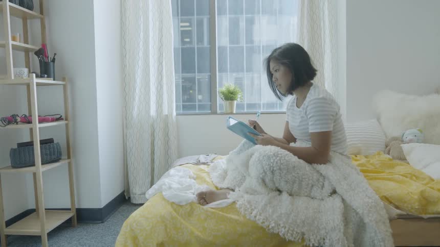 A woman writes in a notebook in bed
