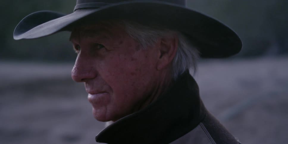 A man in a cowboy hat looks around smiling