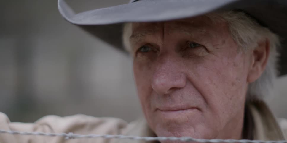 A cowboy stands next to a barbed wire fence