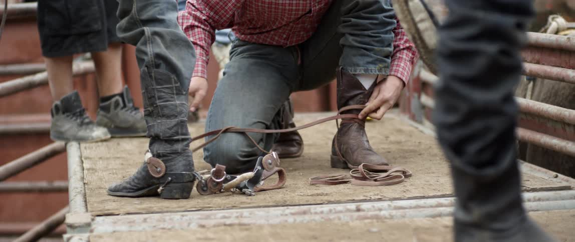 A cowboy wraps leather straps around his boots