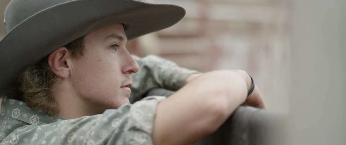 Cowboy watching something as he leans on a high railing