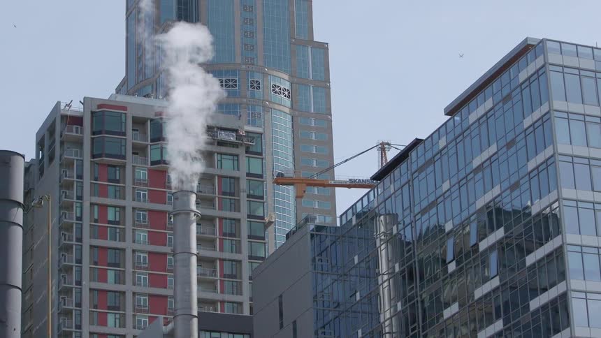 Smoke rises from a smokestack near skyscrapers
