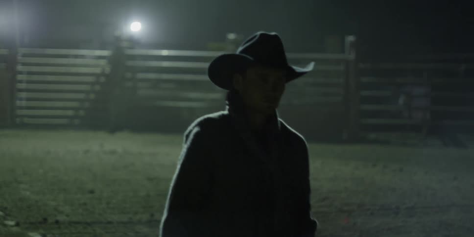 Cowboy walking across a dimly lit corral