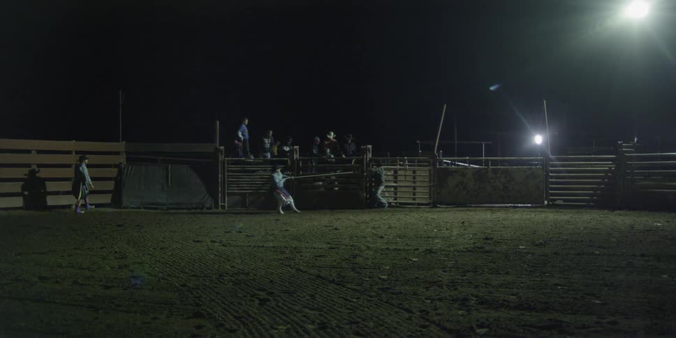 A cowboy rides a bull at night