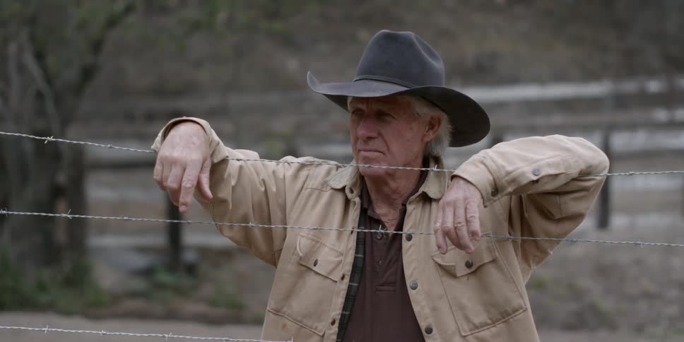 A cowboy rests his arms on a barbed wire fence
