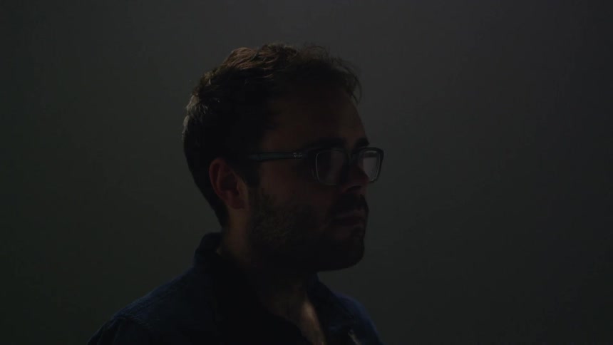 A man stares forward in a dim room