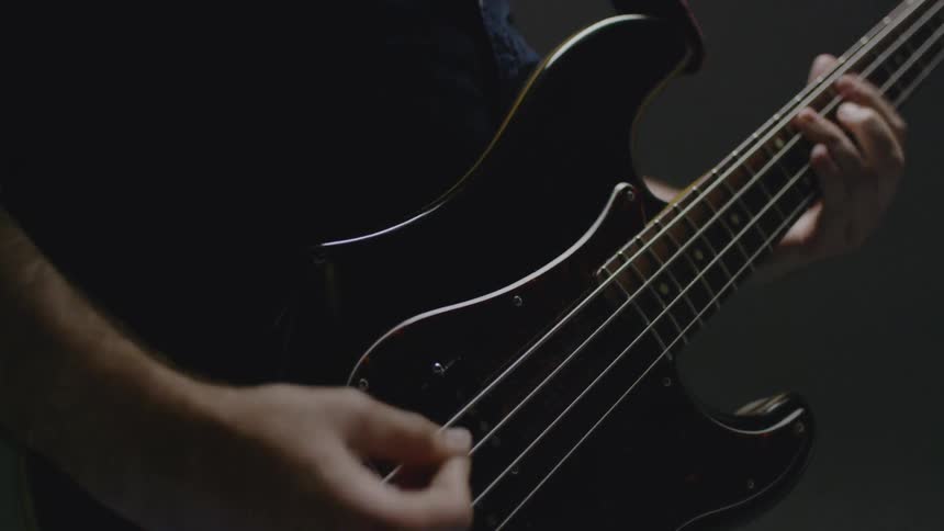 A bassist plays a bass guitar in a dim room
