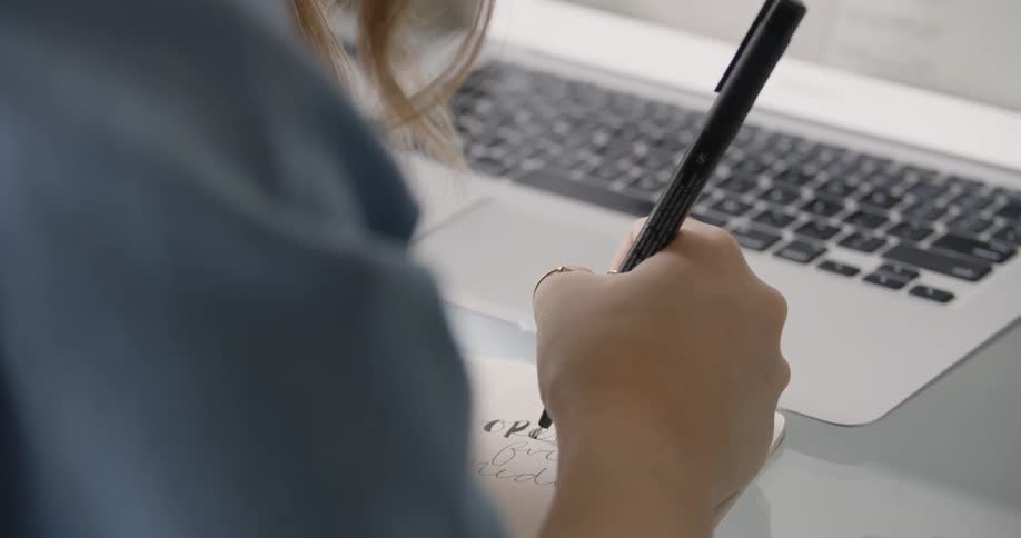 Female College Student Artist is writing in front of her opened laptop
