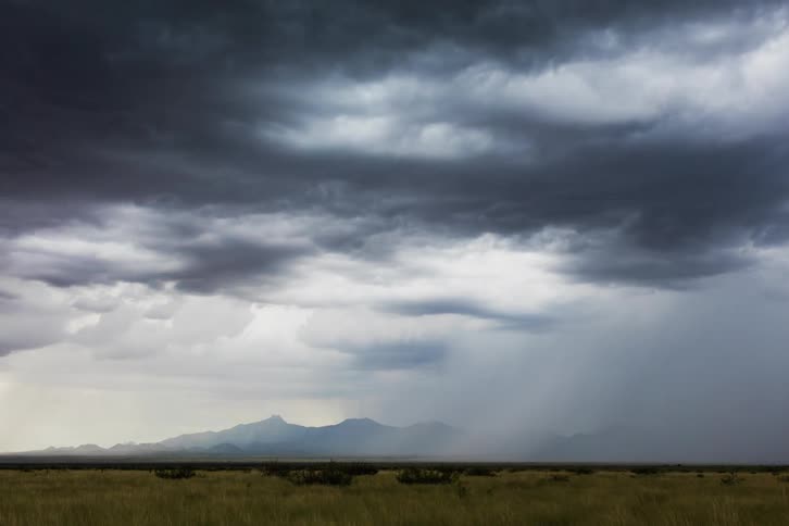 Storm clouds and rain move over peaks and field