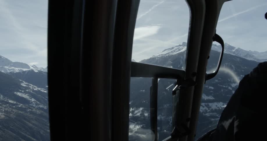 A person is piloting a helicopter above a mountain range on a sunny day