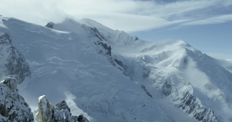 Clouds are drifting over a snow-covered mountain range in daylight