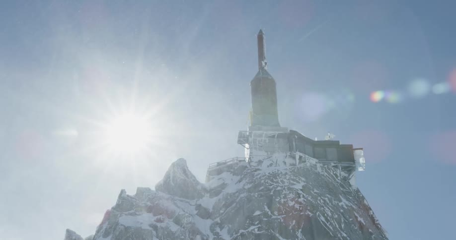 Sun shines over a rocky snowy hilltop an a building