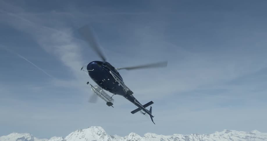 A helicopter takes off near snow covered peaks