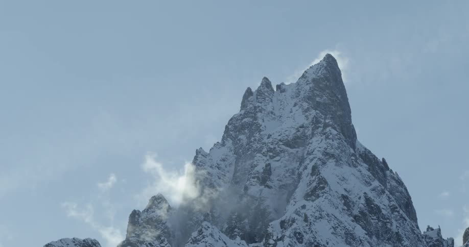 Snow and ice cover the backlit mountain on windy day