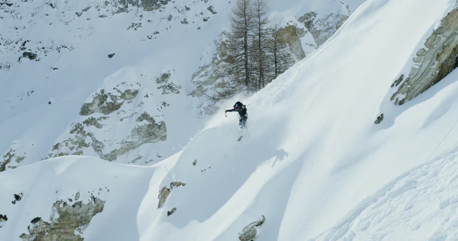 A skier is skiing down a mountain ridge during the day